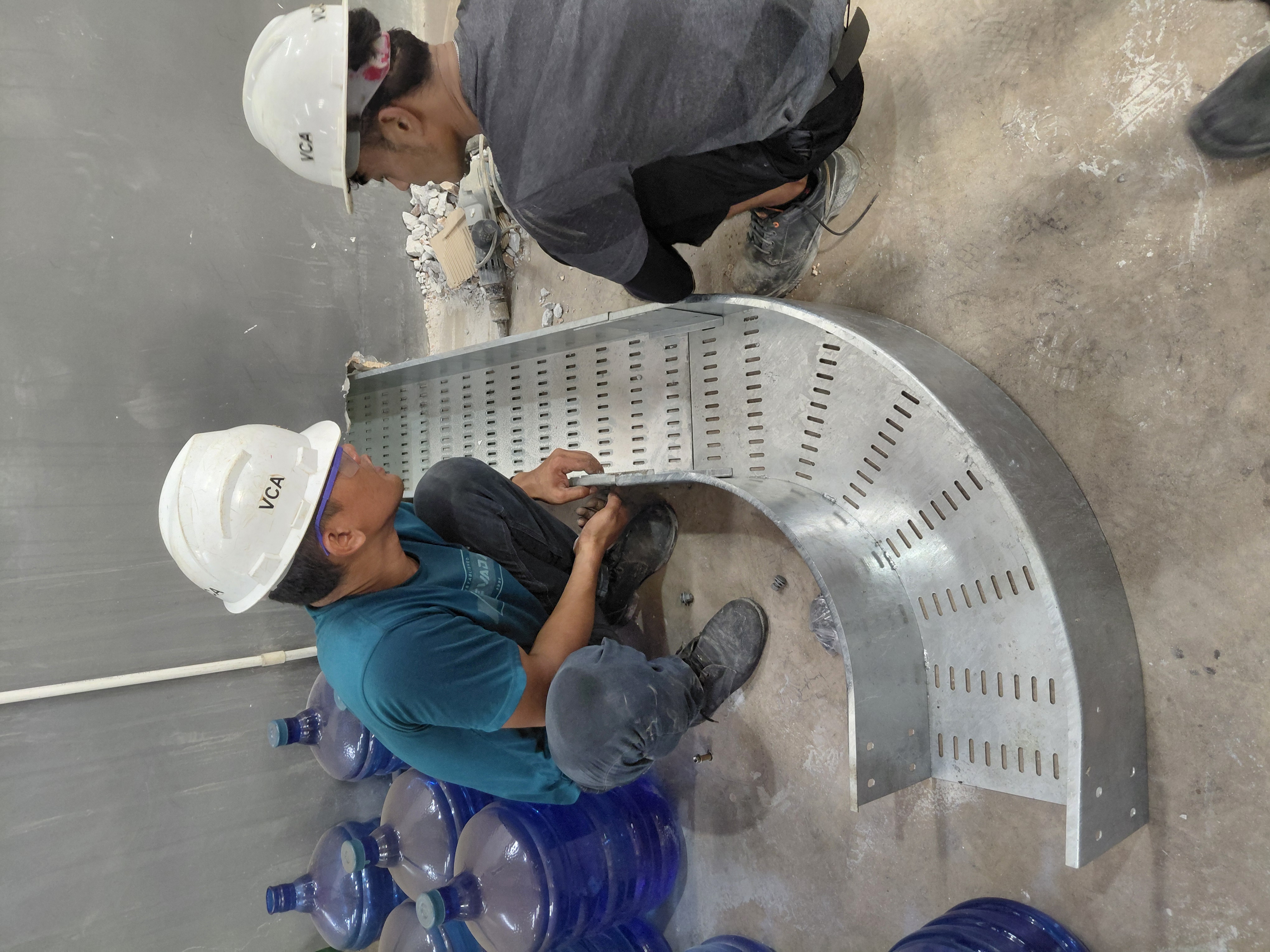 Dua teknisi merakit cable tray metal berbentuk lengkung